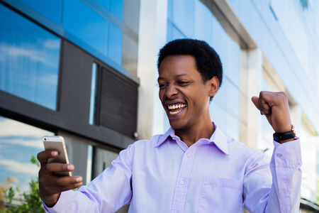 Successful professional young businessman excited with smartphone outside office building. Businessman enjoys success in job.の写真素材