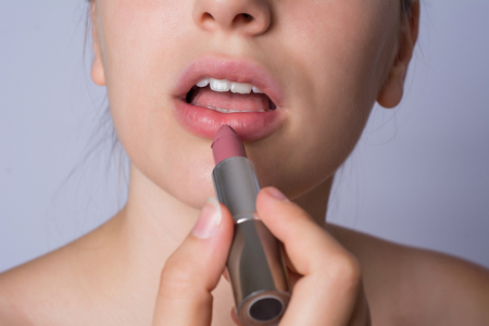 Close-up of young woman applying lipstick on studio.の写真素材