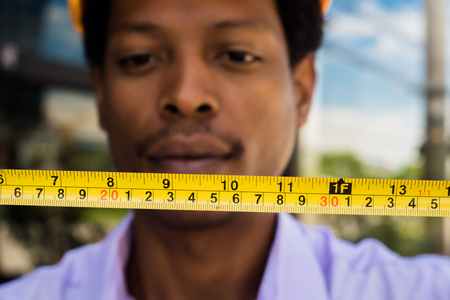 Professional architect in hard hat with measuring tool outside modern building.