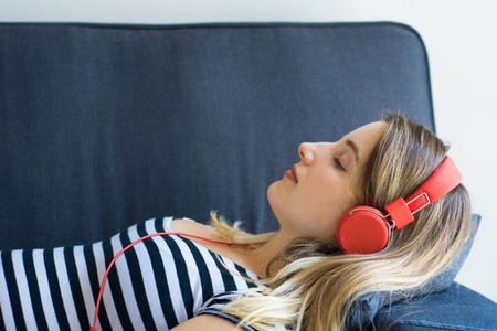 Portrait of attractive woman listening to music while lying on sofa in living roomの写真素材