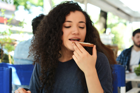 Portrait of young beautiful woman eating a toast while having breakfast at a coffee shop.