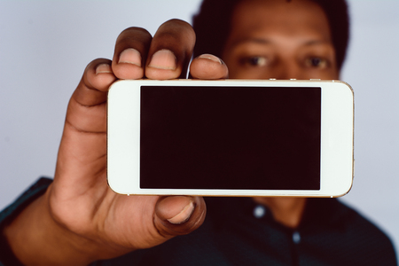 Portrait of Afro American man holding mobile smartphone with black screen on studio.の写真素材