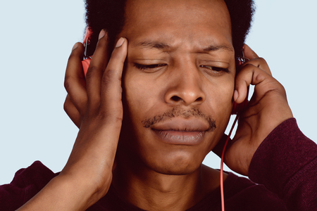 Portrait of Afro American man listening music with red headphones on studio.