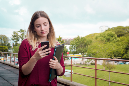 Portrait of a young student outside of university with smartphone.の写真素材
