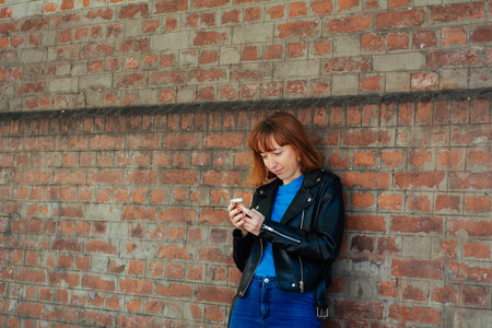 beautiful young redhead woman sending message with smartphone on the street.