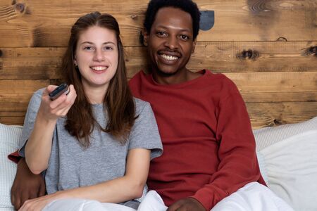 Close-up of Multiracial couple watching tv in a comfortable bed at home.の写真素材