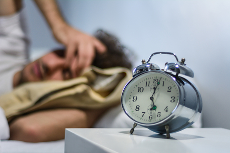 Young latin man hates waking up early in the morning with alarm clock. Indoors.の写真素材