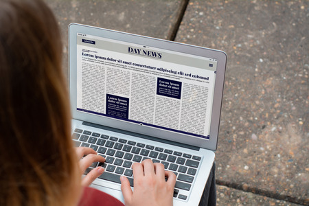 Closeup of young woman reading Breaking News on laptop. Digital newspaper concept. All screen graphics are made up by usの写真素材
