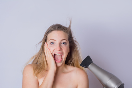 Portrait of young happy woman drying her hair with dryer on studio.の写真素材