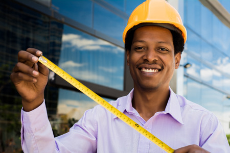 Professional architect in hard hat with measuring tool outside modern building.の写真素材