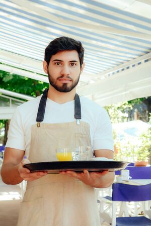 Handsome young waiter holding tray at the coffee shop. Service conceptの写真素材