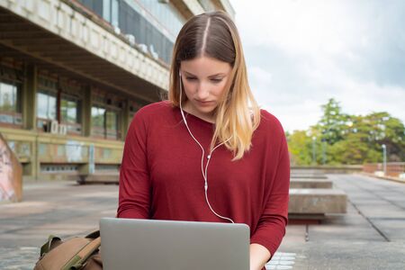 Portrait of young female student using laptop computer outdoors. Education concept