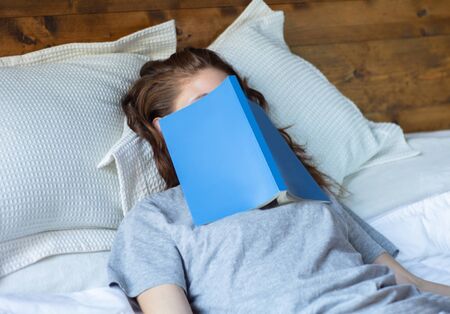 Young red head woman sleeping on bed with book covering her face.