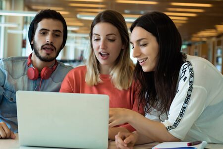University students sitting together at table using laptop. Group study in university library....
