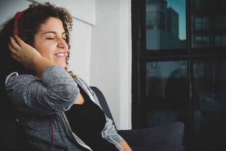 Portrait of attractive woman listening to music while lying on sofa in living room