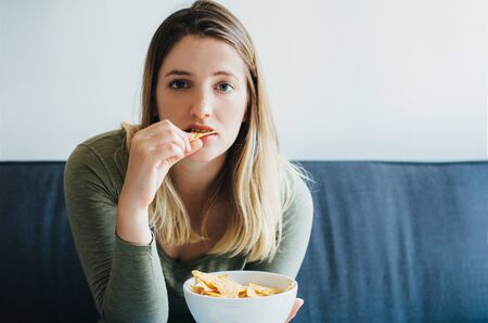Young woman eating snacks and watching the tv on the couchの写真素材