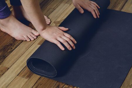 Close-up of attractive young woman rolling her fitness mat before or after yoga class at home. Healthy life concept.の写真素材