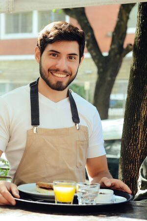 Handsome young waiter holding tray at the coffee shop. Service conceptの写真素材