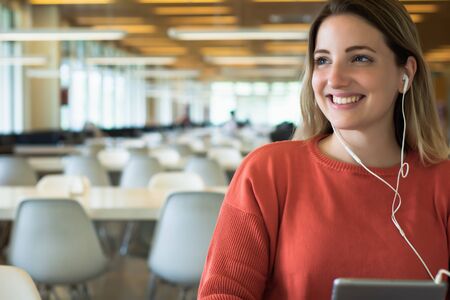 Portrait of young female student with earphones using digital tablet in the university library.の写真素材