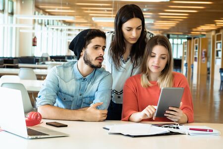 University students sitting together at table using digital tablet. Group study in university...