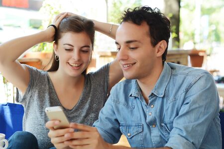Young beautiful couple using smartphone in coffee shop.の写真素材