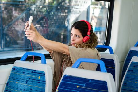 Casual young woman taking a selfie on train with her phone. Enjoying travel.