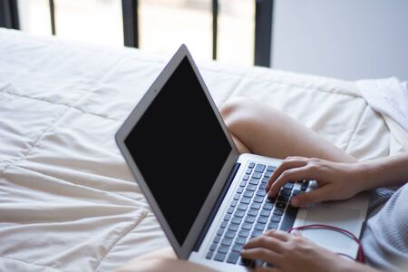 Young woman usign her laptop with black screen while lying on the bed at home.  Lifestyle concept