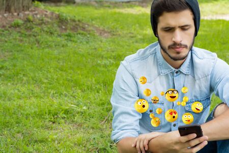 Young latin man using smartphone sending emojis. Social concept.の写真素材