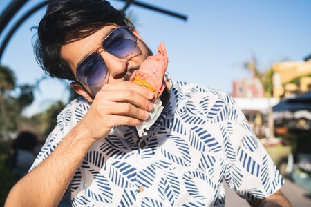 Portrait of young man enjoying sunny weather while eating an ice cream outdoors.
