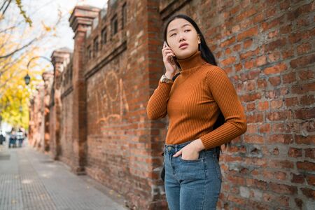 Portrait of young Asian woman talking on the phone outdoors in the street. Urban and communication concept.の写真素材