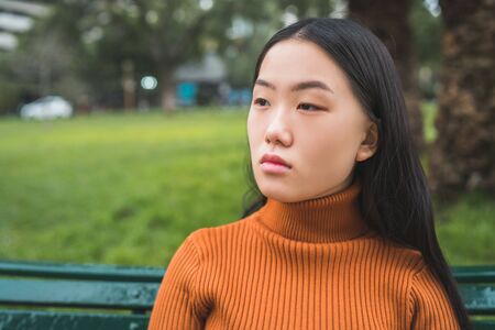 Portrait of young beautiful Asian woman sitting on a bench in the park outdoors.の写真素材