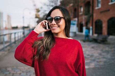 Portrait of young latin woman talking on the phone outdoors in the street. Urban concept.の写真素材
