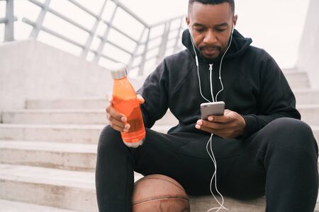 Portrait of an athletic man using his mobile phone on a break from training while sitting on concrete stairs. Sport and health concept.の写真素材