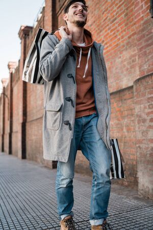 Portrait of young handsome man holding shopping bags while walking on the street. Urban, shop...