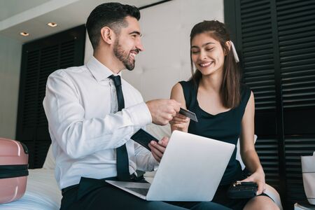 Portrait of two young business people buying flight tickets with laptop and credit card at hotel room. Business travel concept.の写真素材