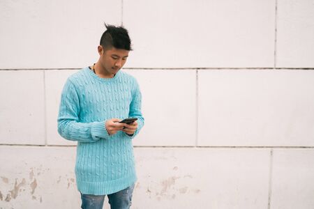 Portrait of young Asian man using his mobile phone standing outdoors in the street. Communication...