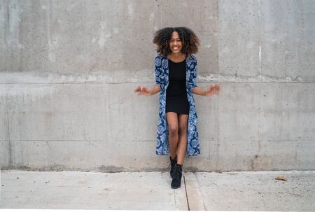 Portrait of beautiful young afro-american woman with curly hair laughing against grey wall.