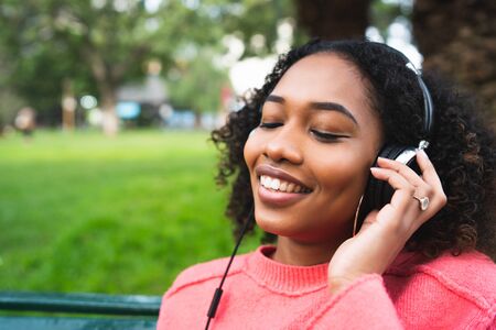 Portrait of Afro american woman smiling and listening to music with headphones in the park....