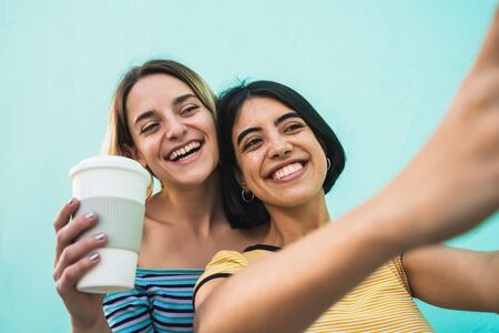 Portrait of lovely lesbian couple having fun and taking a selfie with mobile phone against light blue background. LGBT concept.の写真素材