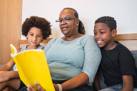 Portrait of African American grandmother reading a book to her grandchildren at home. Family concept.の写真素材