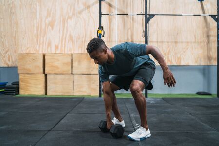 Portrait of young crossfit athlete doing exercise with dumbbell at the gym. Crossfit, sport and...