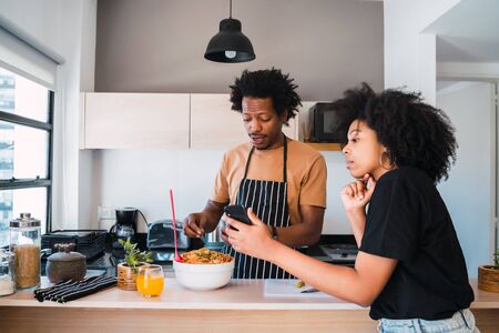 Portrait of young afro couple cooking together and using mobile phone in the kitchen at home....