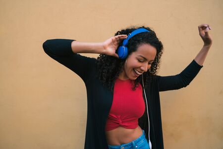 Portrait of young afro woman enjoying and listening to music with blue headphones. Technology and lifestyle concept.の写真素材