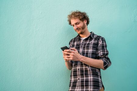 Portrait of young man using his mobile phone against blue background. Communication concept.