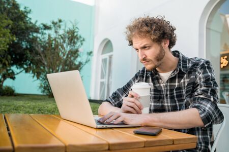 Portrait of young man using his laptop while sitting in a coffee shop. Technology and lifestyle concept.の写真素材