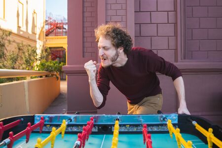 Portrait of young caucasian man having fun and playing table football.