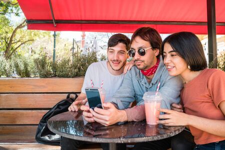 Portrait of three friends spending good time together and taking a selfie with mobile phone at...