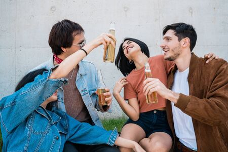 Portrait of young group of friends spending good time together and drinking beer while sitting...