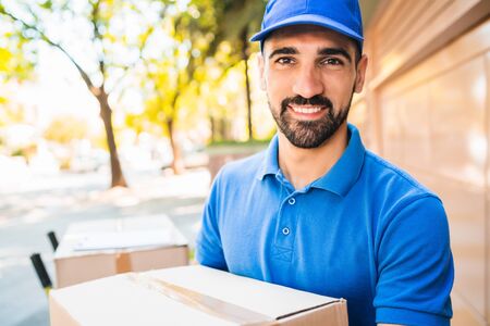 Portrait of a delivery man courier with cardboard boxes in hands outdoors. Delivery and shipping concept.の写真素材