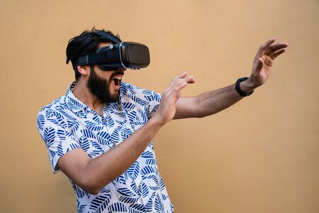 Portrait of young man playing with VR-headset glasses of virtual reality against yellow background. VR headset glasses device. Technology concept.の写真素材